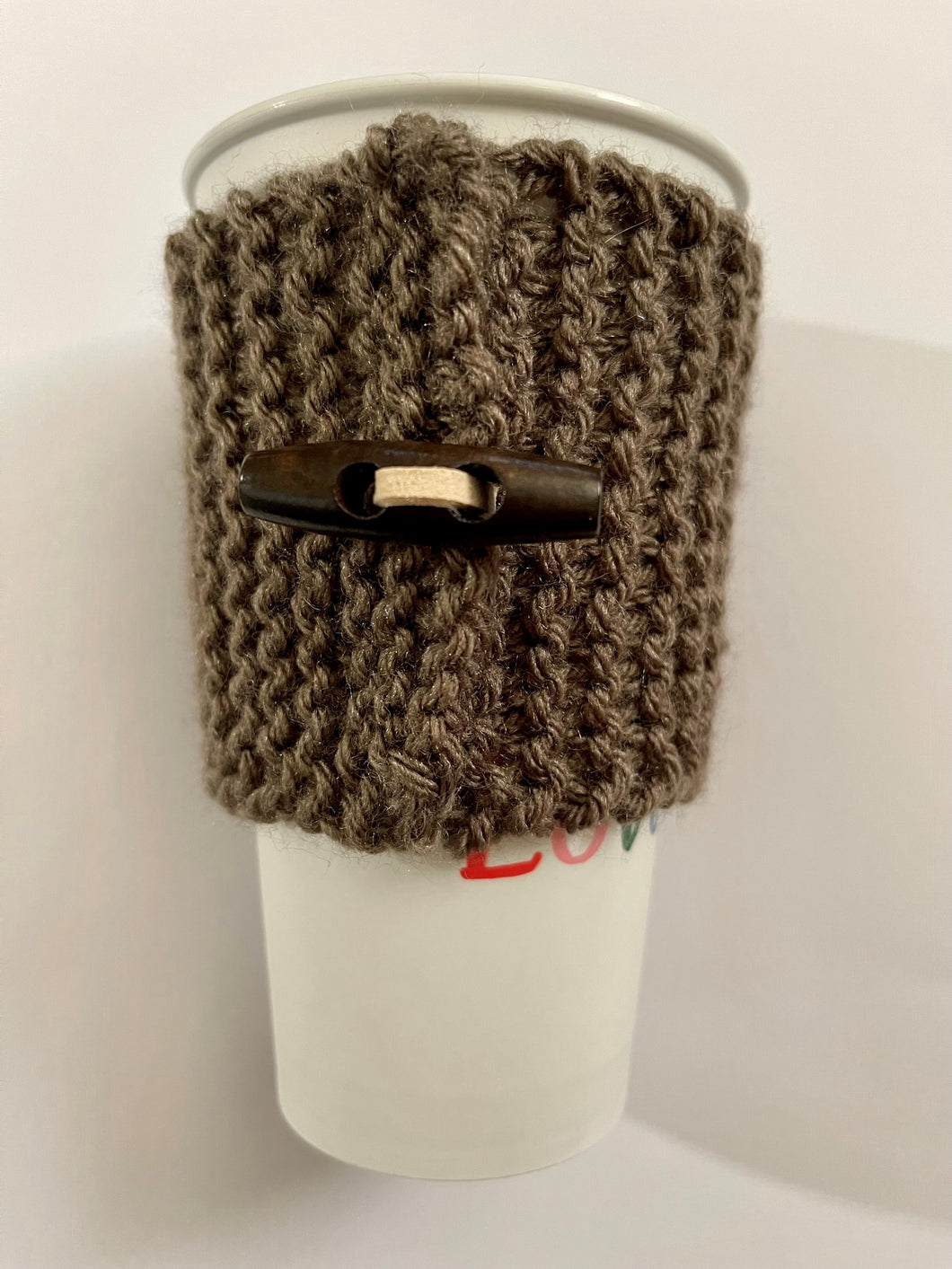 Hand knitted dark brown coffee koozie with dark brown wood toggle button for decoration.