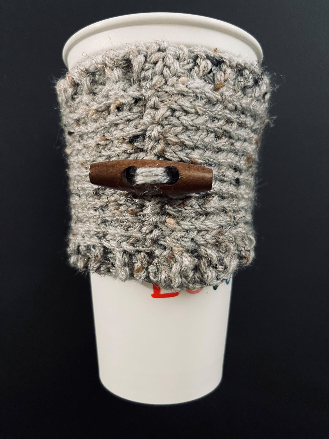 Hand knitted gray coffee koozie with wood toggle button for decoration.