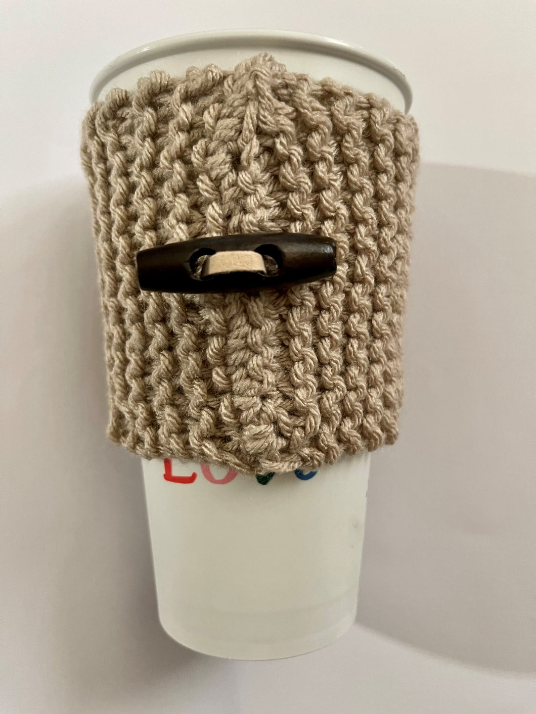 Hand knitted light brown coffee koozie with wood toggle button for decoration.