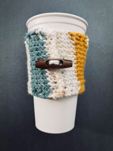 Hand knitted coffee koozie with beige, mustard, green and black with wood toggle button for decoration.